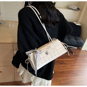Detail of cream checkered shoulder bag featuring bow knot and heart pendant accessory