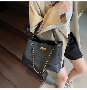 Close-up of black quilted tote bag with golden chain and clasp on wooden stairs