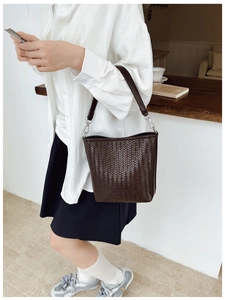 Détail du sac seau marron foncé tressé avec bandoulière en cuir et boucles métalliques