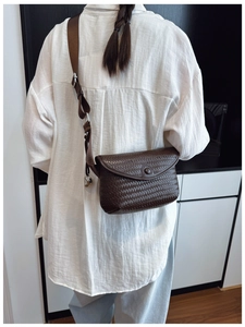 Détail d'un sac bandoulière en cuir tressé marron foncé avec rabat et bouton pression