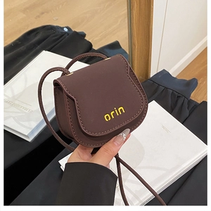 Close-up of a mini dark brown leather saddle bag with yellow orin logo detail