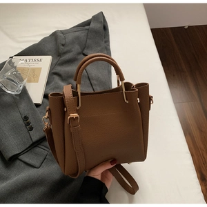 Detail of caramel brown litchi grain leather bucket bag with gold hardware and side wings