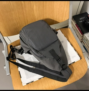 Detail of dark grey nylon crossbody bag with zipper compartments on wooden chair