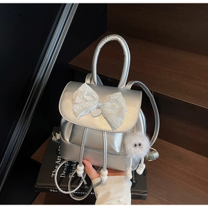 Macro detail of silver mini backpack with white lace bow and plush charm on black book