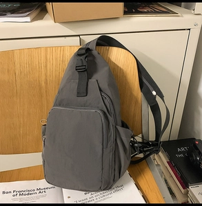Detail view of dark grey nylon multi-pocket crossbody bag on a wooden chair