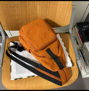 Close-up of orange nylon crossbody bag with zipper pockets and a wide black strap