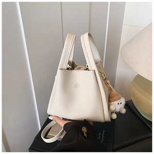 Close-up of cream-white pebble leather bucket bag with gold hardware and plush charm