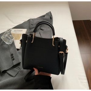 Detailed view of black litchi texture leather bucket bag with gold cylindrical handle hardware