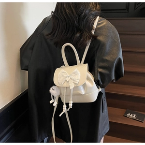 Detail of cream backpack featuring a large lace bow and fluffy monster charm