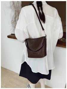 Détail d'un sac seau tressé marron foncé avec poignée en cuir et bandoulière réglable