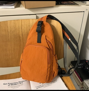 Detailed view of orange nylon crossbody bag with multiple zip pockets on a wooden chair