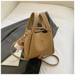 Close-up of khaki pebbled leather bucket bag with plush charm on white bedding