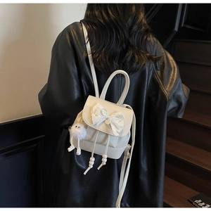 Detail of a beige mini backpack with lace bow and plush charm on a black leather jacket