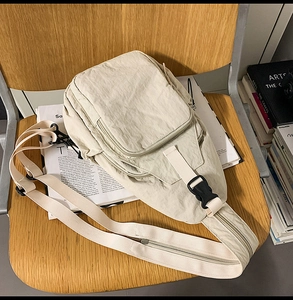 Detail of beige nylon crossbody bag with multi-zipper pockets on a wooden chair