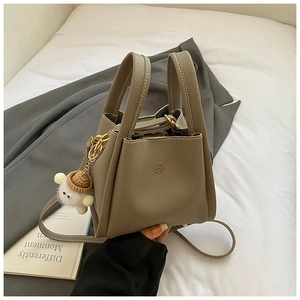 Detailed view of gray pebbled leather bucket bag with cute sheep charm on white linen