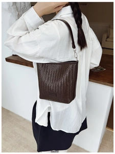 Détail d'un sac seau tissé marron foncé avec boucle argentée porté par un mannequin en scène