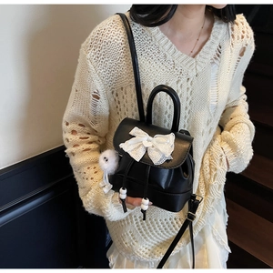 Close-up of mini black backpack featuring white lace bow and plush pendant on model