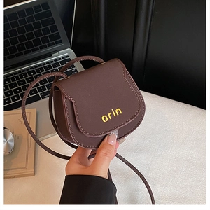 Detailed close-up of dark brown leather mini saddle bag with orin text held by hand