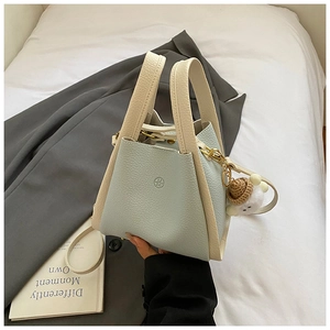 Detail of light blue bucket bag with pebble leather texture, round logo, and doll charm