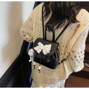 Close-up of mini black PU leather backpack with white lace bow and plush monster charm