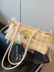 Yellow and white checkered shoulder bag with lace trim and bow detail held by hand