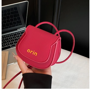 Detail of rose red mini saddle bag featuring yellow orin logo and textured leather finish