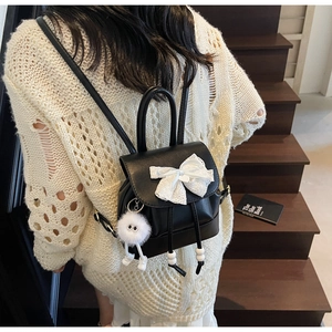 Detail of black PU leather mini backpack with lace bow and plush charm on stairs