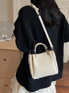Chic beige lychee leather bucket bag with top handle and gold logo in a modern setting
