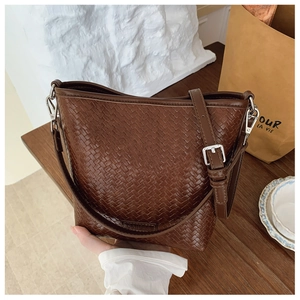 Détail d'un sac seau tressé marron montrant le cuir artisanal et la boucle argentée