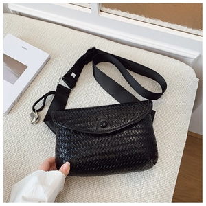 Détail du sac bandoulière tressé noir avec rabat rond et breloque en métal argenté