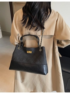 Black quilted tote bag with gold chain strap worn with a stylish beige trench coat