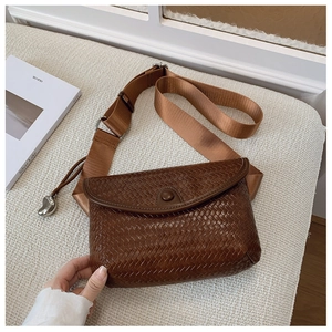 Détail d'un sac bandoulière tressé marron foncé avec pendentif coeur et large sangle