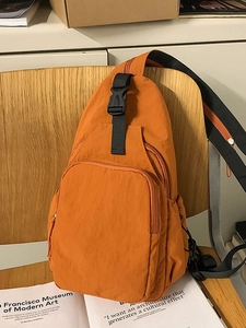 Orange nylon multi-pocket crossbody bag with adjustable black strap on wooden chair