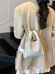 Blue and beige bucket bag with bear charm shown on model in a minimalist setting