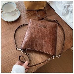 Vue détaillée du sac seau marron à texture tressée avec bandoulière et logo de la marque