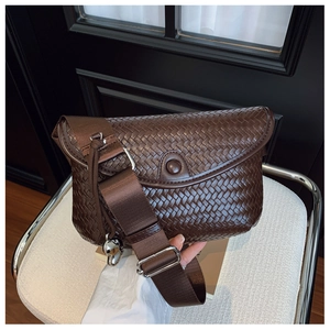 Détail d'un sac à bandoulière tressé marron foncé avec large sangle et breloque ours