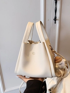 Minimalist white bucket bag in lychee leather with dual handles and plush charm