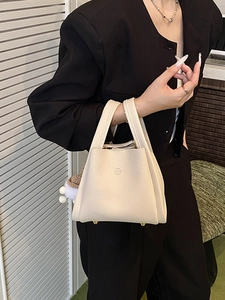 Minimalist beige pebble leather bucket bag with top handles and decorative charm