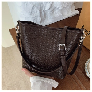Détail d'un sac seau tressé marron foncé avec bandoulière réglable et boucles argentées