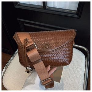 Détail d'un sac à bandoulière tressé marron avec breloque cœur et sangle réglable