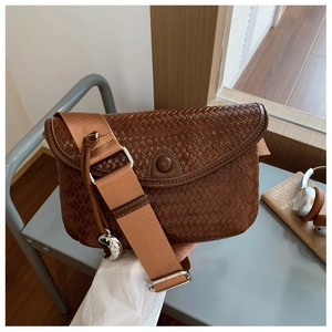 Détail d'un sac bandoulière marron tissé avec large sangle dans un décor décontracté