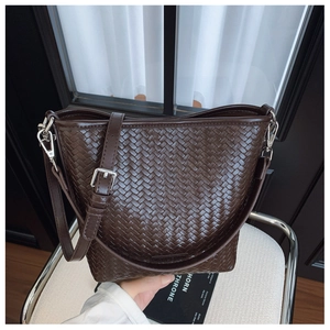 Détail d'un sac seau en cuir tressé marron foncé avec bandoulière réglable sur chaise