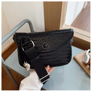 Détail d'un sac bandoulière tressé noir avec large sangle et pendentif cœur argenté
