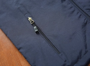 Detalle de cerca del bolsillo con cremallera de bronce del chaleco azul con tirador de marca