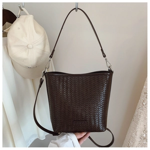 Détail d'un sac seau tressé en cuir marron foncé avec ferrures argentées et deux anses
