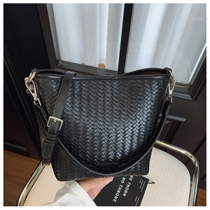 Détail d'un sac seau noir tressé avec bandoulière réglable et boucle métallique argentée