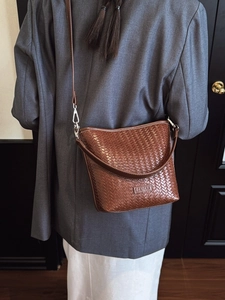 Sac seau marron à texture tressée porté par un mannequin sur un blazer sombre