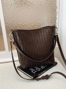 Sac seau marron à texture tressée avec bandoulière réglable et logo sur un livre décoratif