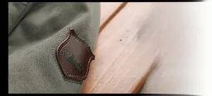 Detailed view of an olive green canvas jacket with an embossed brown leather mountain patch