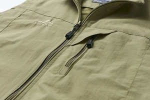Détail macro du gilet extérieur vert olive avec zip et broderie de montagne